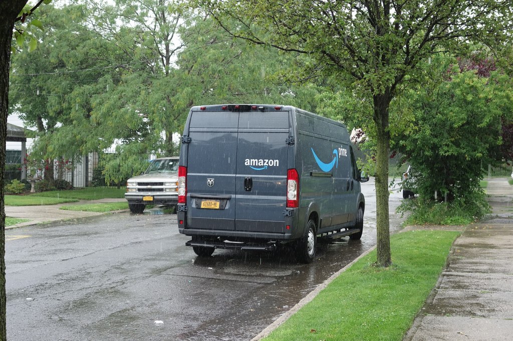 A gray Amazon Prime delivery van parked on a rain-wet residential street in Hillcrest, Queens