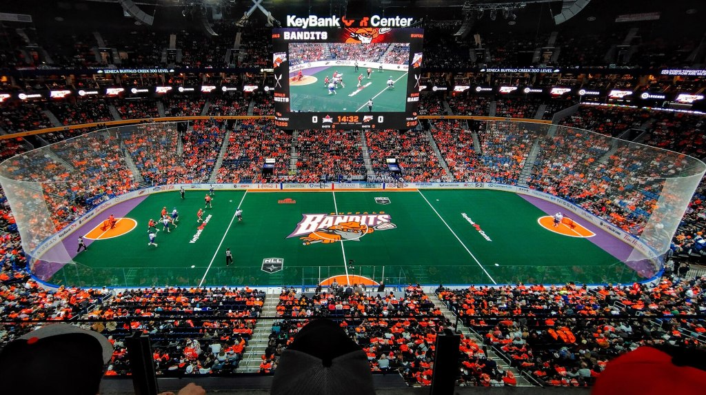 A box lacrosse game on green turf before an orange-clad crowd at Buffalo's KeyBank Center