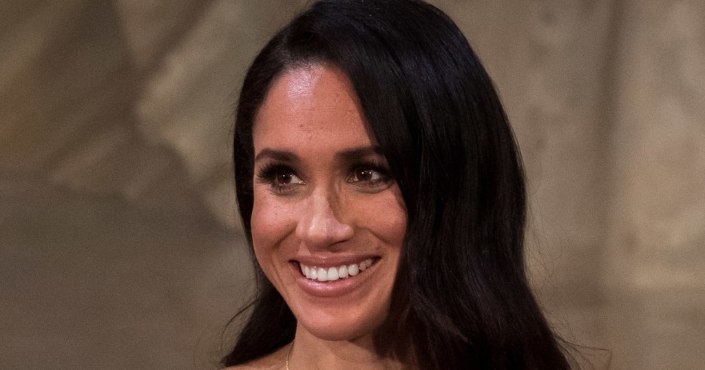 Meghan, Duchess of Sussex, smiling at a microphone in a black off-the-shoulder dress at an official reception in New Zealand, October 2018